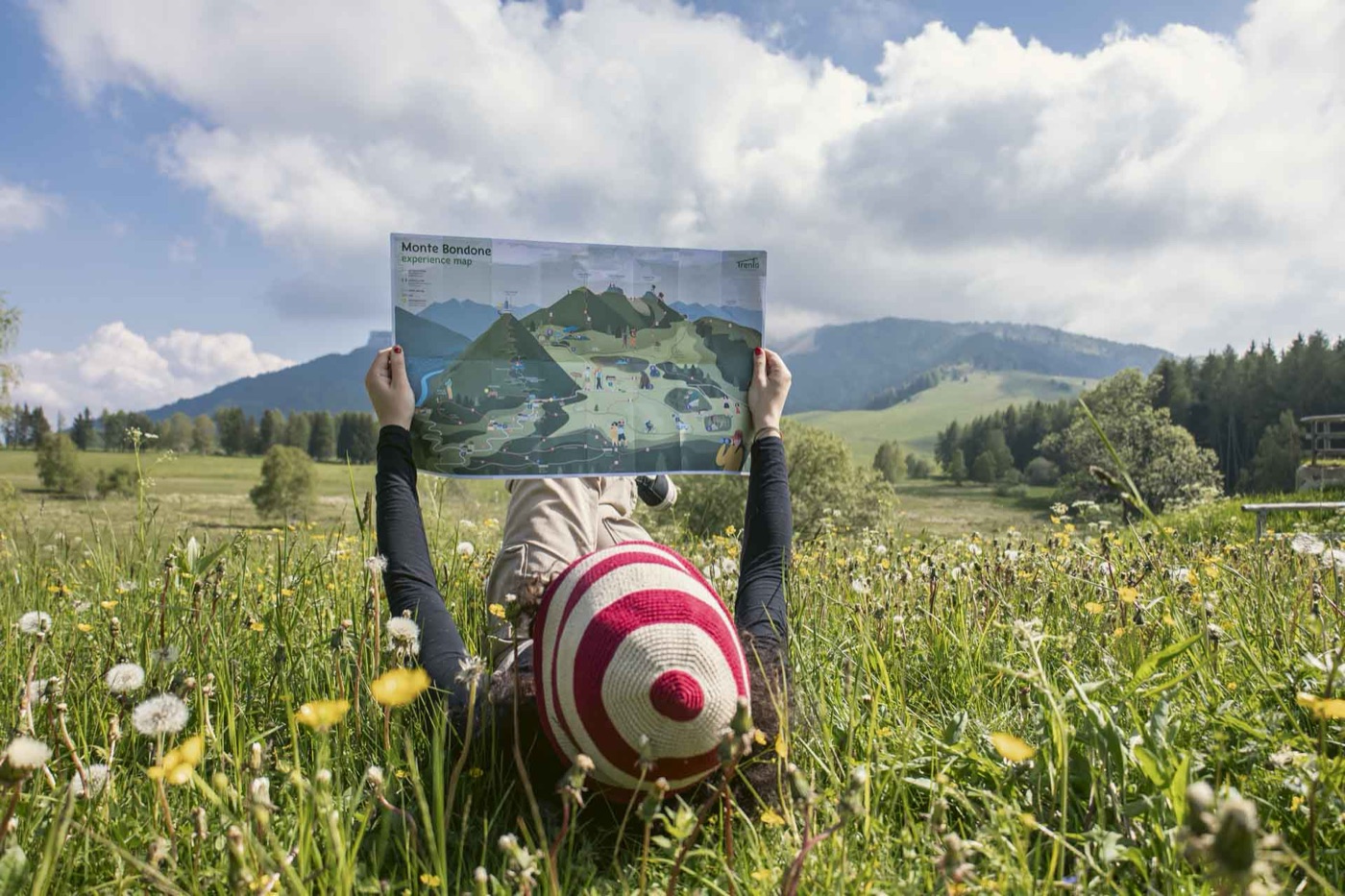 Una ragazza nel prato legge la mappa del Bondone