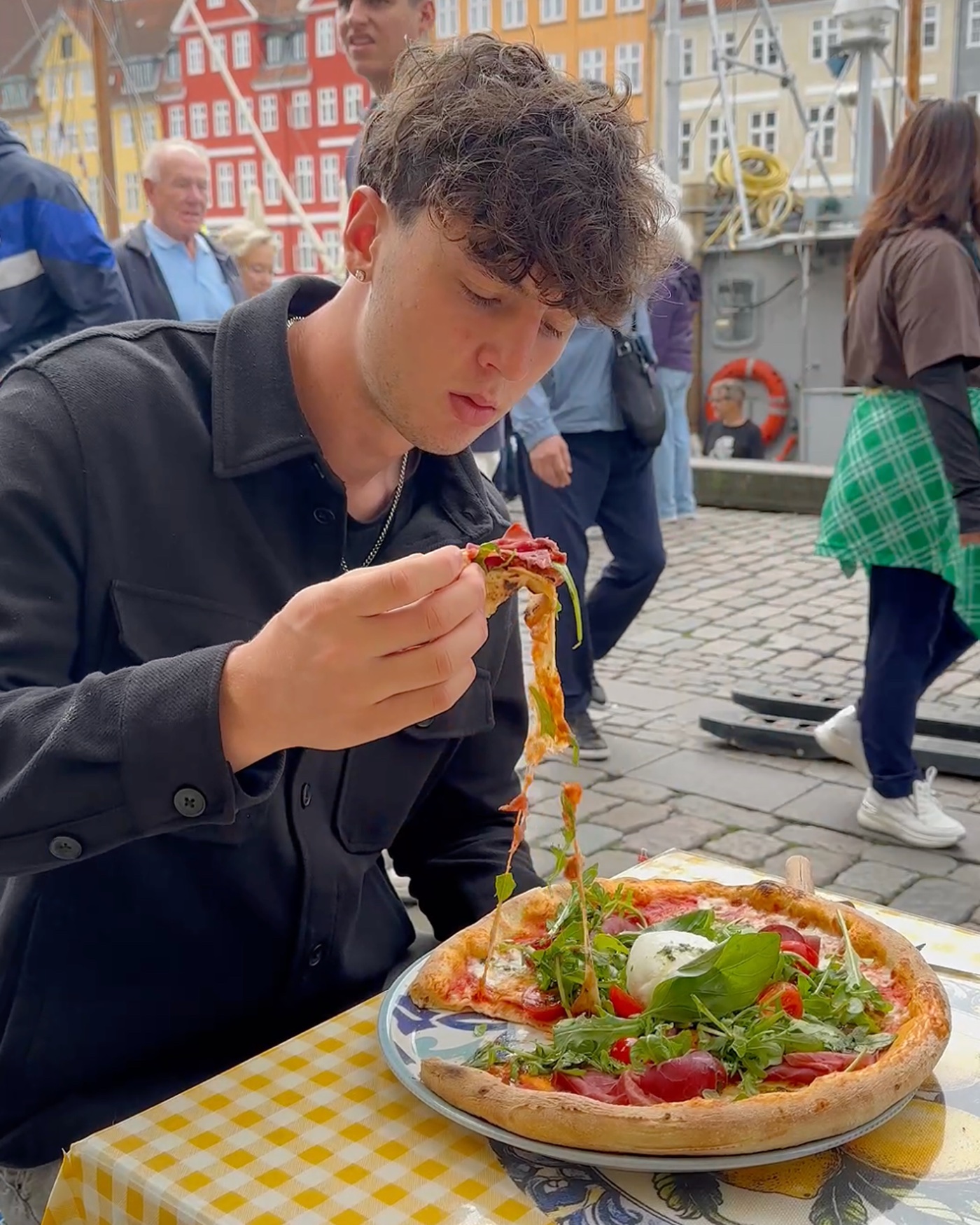 Un ragazzo mangia la pizza al tavolo fuori, sul canale di Nyhavn