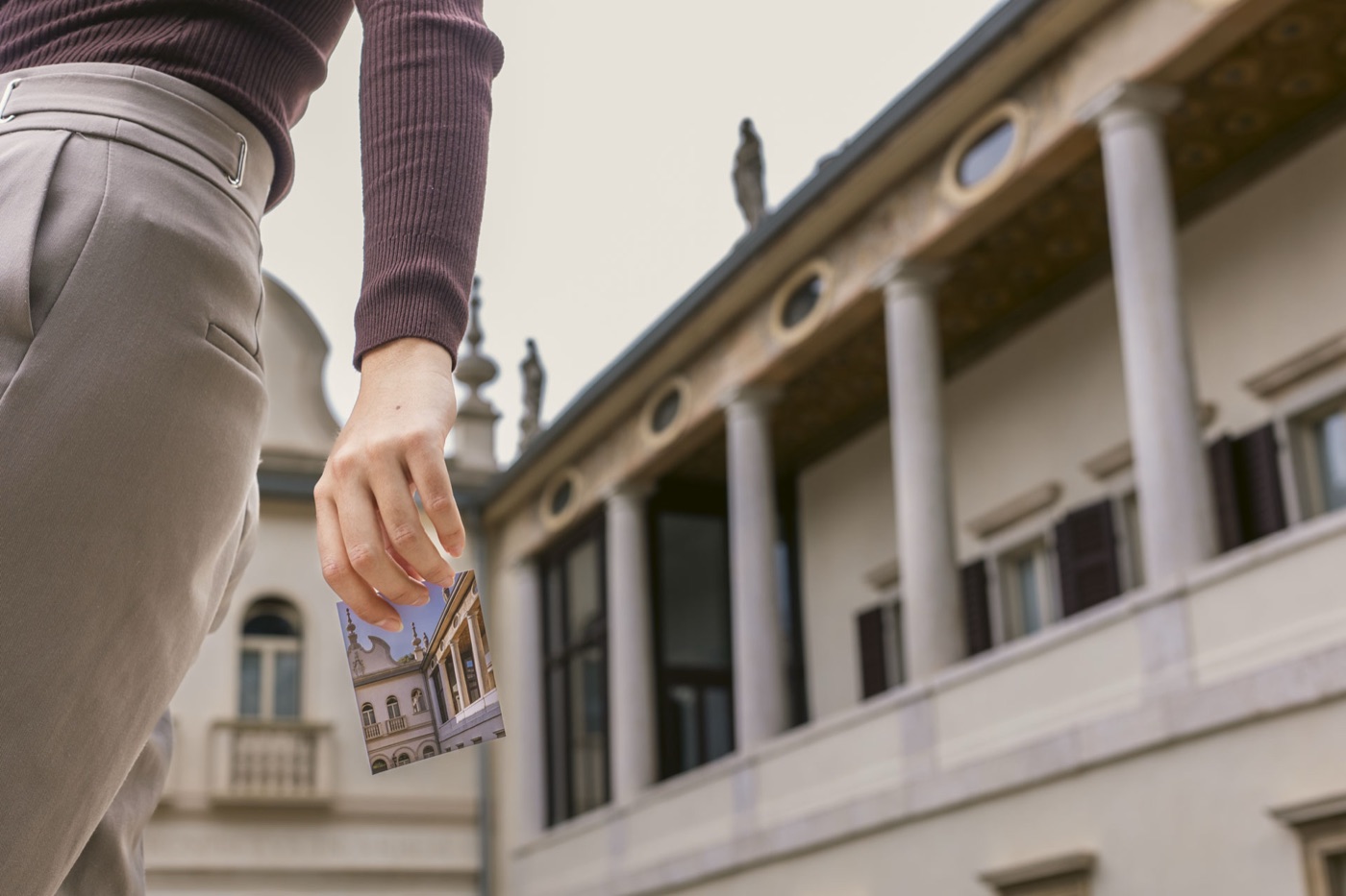 Il loggiato con le colonne di Villa Sizzo e una mano che tiene una cartolina della villa
