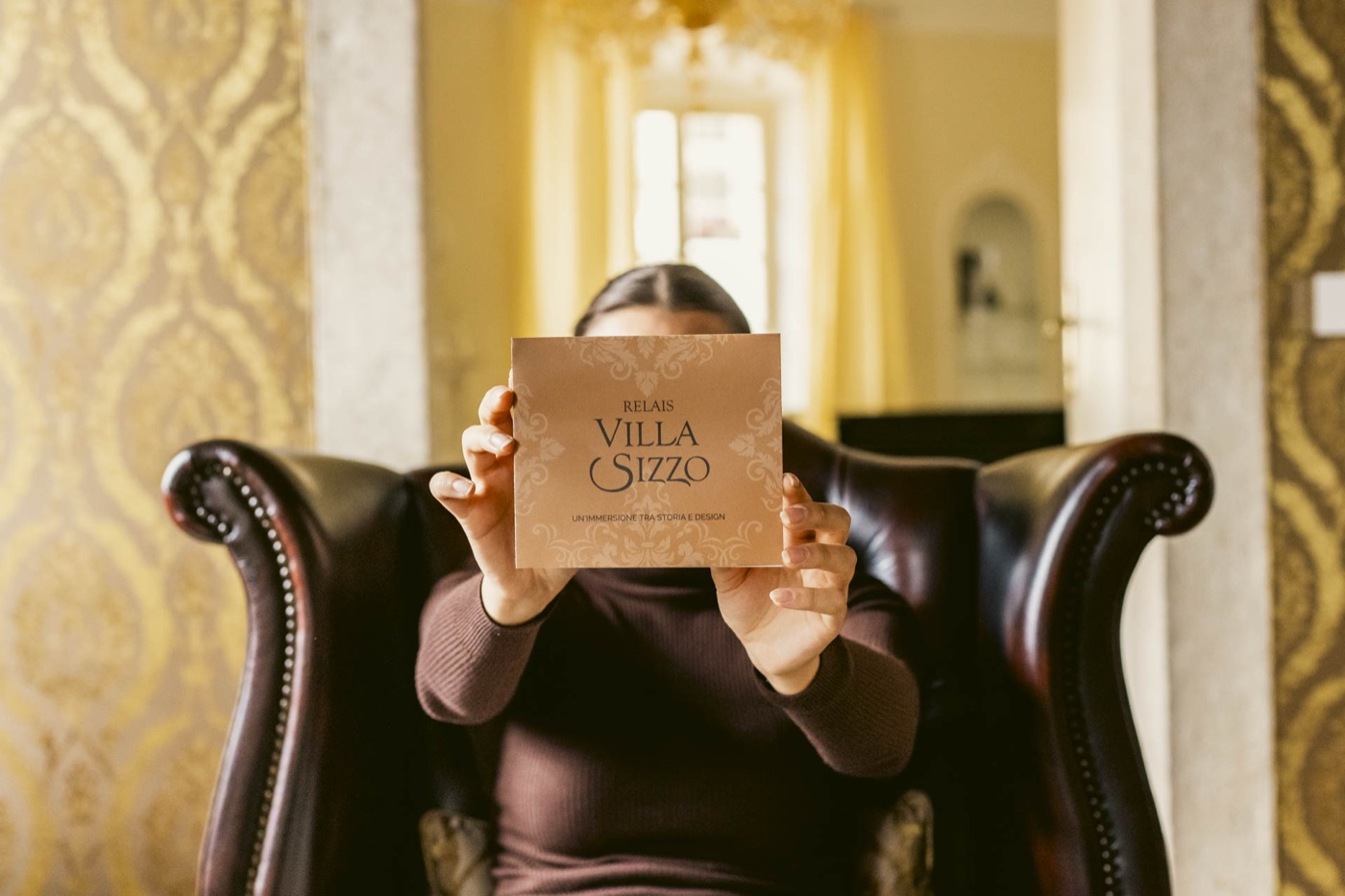 Una ragazza tiene la brochure davanti al viso, seduta in poltrona